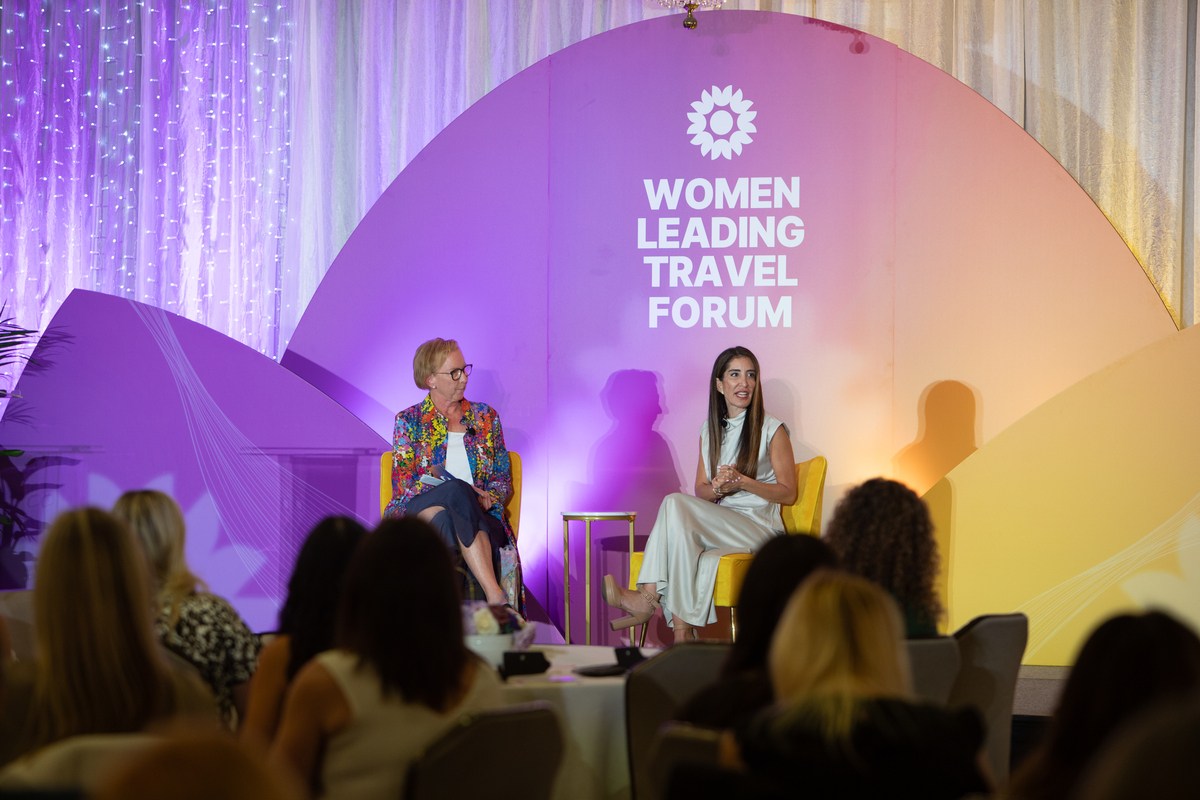 Two speakers in conversation on stage at the Women Leading Travel Forum, seated in yellow armchairs before an audience